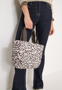 Sac fourre-tout à imprimé léopard en tissu doux, doté de deux poignées robustes et d'une forme structurée. Les tons neutres dominent le motif.