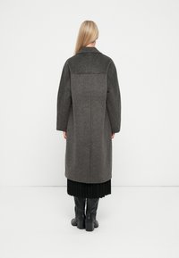Grijze wol coat met een ingelijkt ontwerp, brede mouwen en een rechte silhoët. Heeft een kraag en valt tot halverwege de kuit over een geplooide rok.
