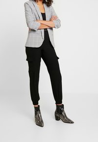 Blazer à carreaux gris avec une coupe ajustée, associé à un pantalon cargo noir fuselé et des bottines à motifs serpent avec un bout pointu.