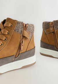Bruna läderankelboots med en grå nedre del, texturerad brun tygovandel, metallblixtlås och snörningsdetaljer; vit gummisula.