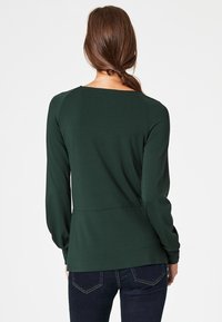 Tmavě zelené tričko s dlouhým rukávem, kulatým výstřihem, úzkým střihem a hladkou texturou. Zadní část má jednoduchý design bez ozdob.