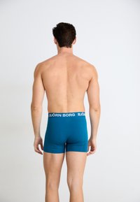 Boxer briefs fitted di colore teal con una cintura nera a contrasto che presenta il testo "BJÖRN BORG". Tessuto liscio e taglio a vita media.