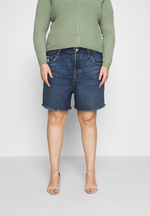 Person wearing frayed hem dark denim shorts, light green ribbed buttoned sweater, and nude ankle-strap heels standing against white background.