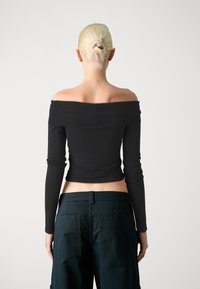 Svart av- skulderen topp med lange ermer, tettsittende design og kort lengde, kombinert med mørke cargo-bukser med flere lommer.