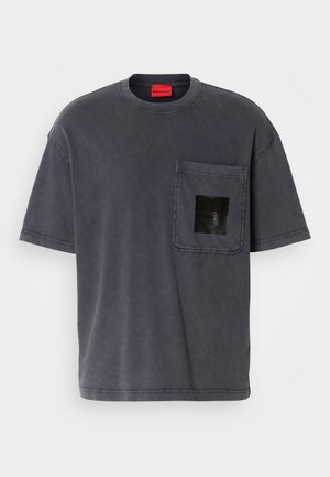 Camiseta de algodão cinza escuro de manga curta com um bolso no peito, apresentando um logótipo quadrado preto e uma etiqueta vermelha da marca dentro da gola.