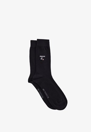 Paire de chaussettes noires montant jusqu'au milieu du mollet avec les lettres « KING » et un motif de cartes près du bord-côte, et le texte « WE FASHION » sur la semelle.