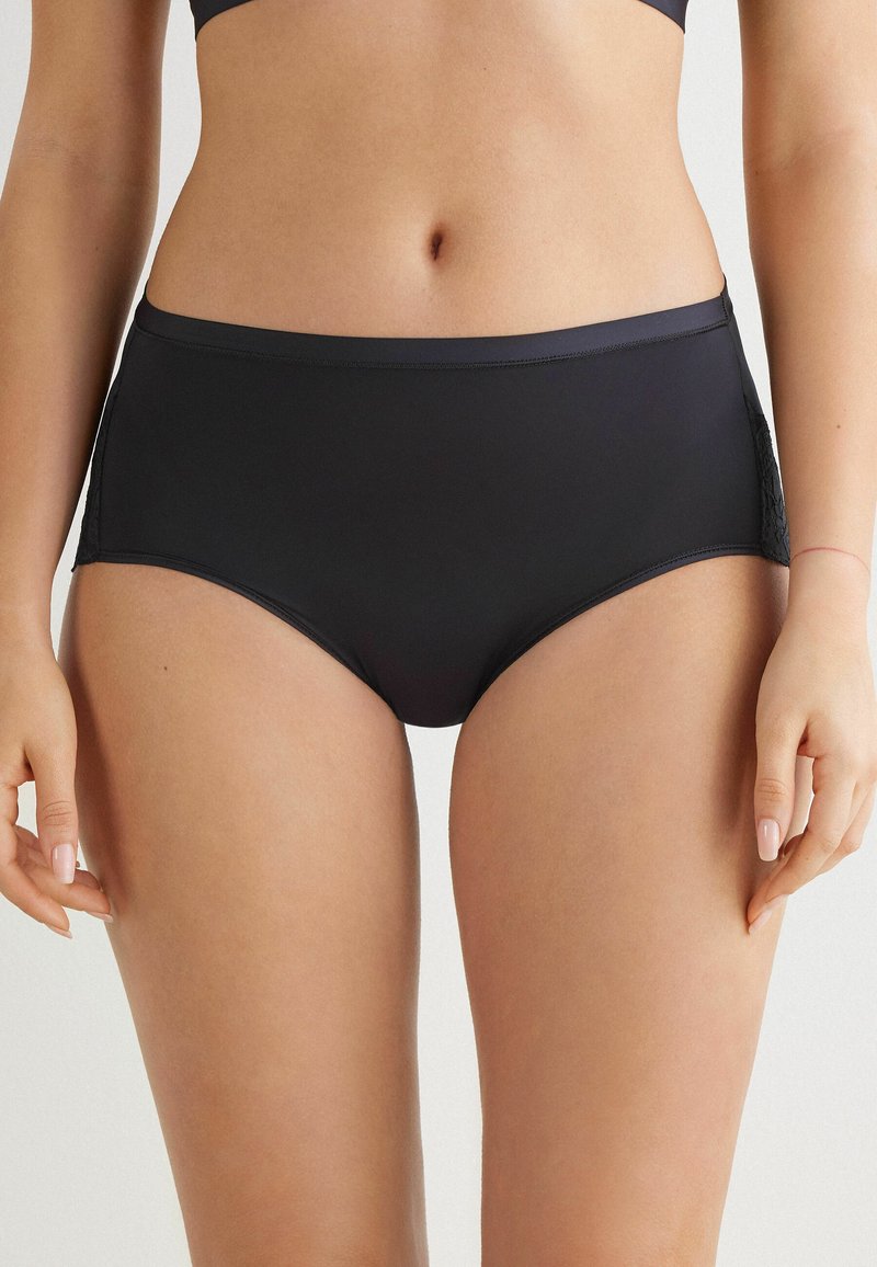 Högmidjade svarta bikiniunderdelar i mjukt tyg med spetsdetaljer på sidorna. Har en enfärgad, ogenomskinlig design och bekväm passform.
