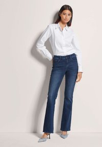 White button-up shirt with long sleeves, paired with dark blue flared jeans and light blue pointy-toed heels. Smooth fabric, classic design.