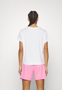 White short-sleeved T-shirt with a crew neckline, paired with pink shorts. Fabric appears soft; shirt has a relaxed fit and simple design.
