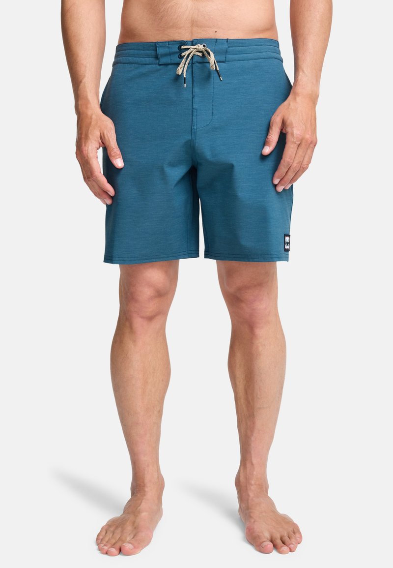 Μπλε μαγιό σορτς με ελαστική μέση και κορδόνι, με επίπεδη μπροστινή όψη, πλαϊνές τσέπες και μικρό λογότυπο.