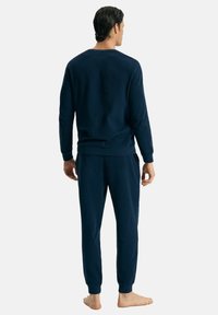 Granatowy komplet odzieży do relaksu z bawełny z dodatkiem innego materiału, o teksturowanym, prążkowanym wzorze. Bluzka ma okrągły dekolt, a spodnie mają elastyczne mankiety.