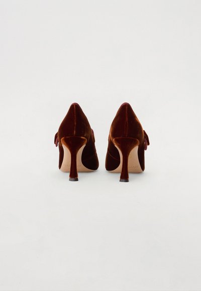 Chaussures à talons hauts en velours rouge foncé avec des pointes et un détail de nœud à l'arrière. Présentent un talon fin et une texture lisse.