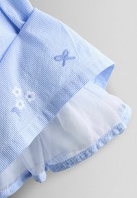 Mėlyna dryžuota medžiaga su baltais gėlių ir juostelių siuvinėjimais. Apatinėje dalyje sluoksniuota permatoma balta tiulis. Apvalus apatinis kraštas ir minkšta tekstūra.