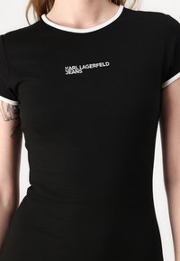 Fekete, testhezálló póló, puha pamutból készült, fehér kontraszt nyakkal és hímzett "KARL LAGERFELD JEANS" logóval az elején.