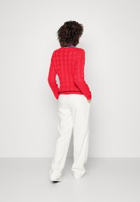 Röd ribbad tröja med texturerat mönster, kombinerad med vita vida byxor. Tröjan har en tajt passform och långa ärmar.