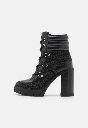 Botte courte à talons hauts noire avec un dessus en tissu texturé, devant lacé, col rembourré et semelle épaisse en caoutchouc. Comprend des œillets et des accents en métal.