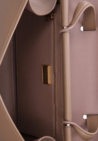 Interno di una borsa a mano in pelle beige, con una tasca con zip dorata, superficie texturizzata e accenti lisci. Due cinture verticali e una placca con il logo sono visibili.
