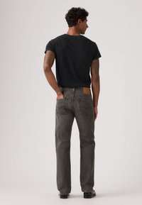 Meeste must T-särk, mida kantakse hallide teksadega, mille vöökohal on nahast detail ning tagataskutel klassikalised õmblused.