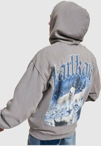 Persona vistiendo una sudadera con capucha gris con un gráfico de lobos blancos en un bosque nevado y la palabra "tartkart" en la parte de atrás.