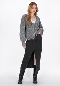 Grå stickad cardigan med ett knyt i fronten, tillsammans med en svart jeanskjol med en framficka, bärs med svarta knähöga stövlar.