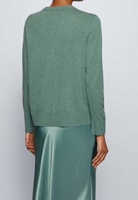 Grön stickad tröja med rund hals och långa ärmar, med ribbad nederkant och muddar. Kombineras med en blanka grön kjol.