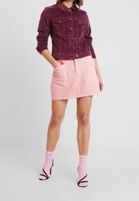 Burgunderrote Cordjacke aus Kord mit Kragen und zwei Brusttaschen, kombiniert mit einem hellrosa Jeansrock mit großen Fronttaschen.