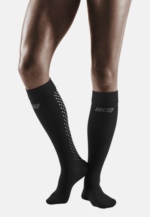 Zwarte compressiesokken met een gestructureerd patroon aan één kant, voorzien van een logo en een gestructureerd voetgedeelte. Glad, rekbaar materiaal.