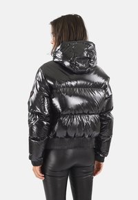 Doudoune noire avec une finition brillante, capuche, poignets et taille côtelés. Présente des sections matelassées horizontales pour l'isolation.