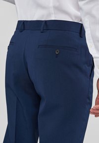 Marina byxor i slät tyg har en skräddarsydd passform, två bakfickor med knappstängning och en ren midjedesign.