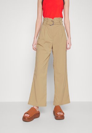 Beige vide bukser med høj talje og bæltestropper med en rund metal spænde. Båret med en rød ribbet tanktop og brune platform sandaler.