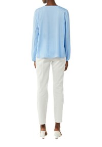Hellblaues Langarmbluse mit geradem Schnitt und rundem Ausschnitt. Kombiniert mit weißen eng anliegenden Hosen und weißen offenen Schuhen. Glatte Textur.