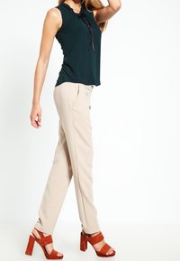 Blusa sin mangas de color verde oscuro con escote en forma de llave, pantalones beige a medida y sandalias de plataforma marrones con tacón grueso.