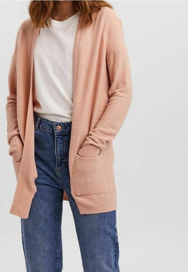 Långärmad, ribbad cardigan i mjuk rosa, med öppen fram, två framfickor och en avslappnad passform, ihop med blå jeans.