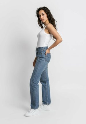 Jeans dritti blu chiaro con tasche frontali e vita alta, abbinati a un top a canotta bianco e sneaker bianche. Denim liscio e resistente.