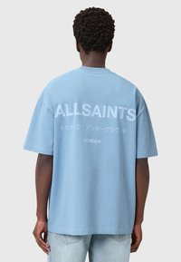 Vaaleansininen puuvillapaita lyhyillä hihoilla, jossa on suuri valkoinen teksti selässä "ALLSAINTS" ja "LONDON." Rennon muotoinen.