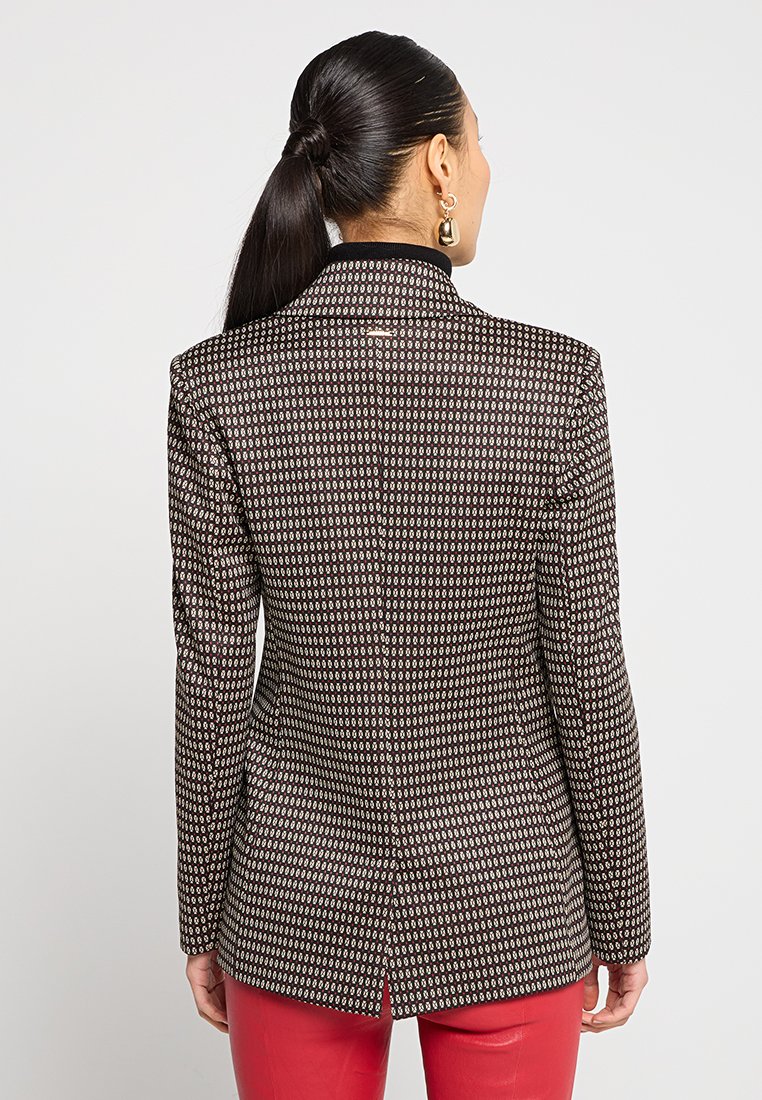 Muster-Blazer in Schwarz, Creme und Rot. Mit strukturierten Schultern, schmaler Passform und einem Schlitz am Rücken für Bewegungsfreiheit.
