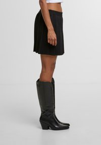 Černá plisovaná mini sukně s elastickým pasem, spárovaná s lesklými černými vysokými botami na kolena s blokovým podpatkem. Čisté linie a texturovaná látka.