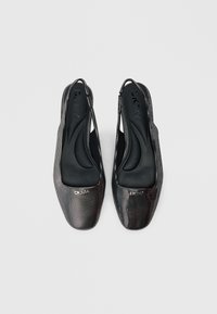 Černé slingback boty s texturovaným povrchem a kovovými detaily. Design se čtvercovou špičkou s logem DKNY na přední části. Hladká vnitřní podrážka.