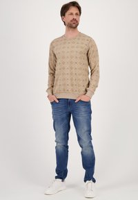 Beige mustriga dressipluus pikade varrukatega, ümmarguse kaelusega, koos siniste teksade ja valgete tossudega. Kujunduses on geomeetrilised kujundid.