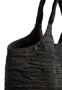 Sac cabas noir texturé avec tissu froncé et doubles poignées, montrant un gros plan de la partie supérieure et des détails de couture sur fond blanc.