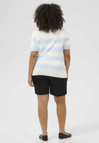 Gestreepte gebreide trui in lichtblauw en wit, gecombineerd met zwarte shorts. Korte mouwen, strakke lijnen en een relaxte pasvorm. Platte zwarte schoenen.