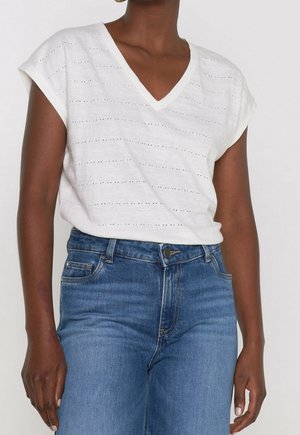 T-shirt blanc à encolure en V avec des rayures texturées et de petits trous, associé à un jean bleu taille haute. Manches courtes retroussées et coupe décontractée.