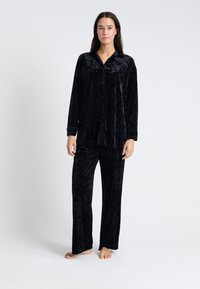Conjunto de pijama de terciopelo negro que incluye una camisa de botones de mangas largas y pantalones a juego, ambos con una textura suave y un ajuste relajado.