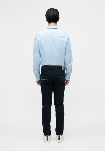 Šviesiai mėlyna ilgomis rankovėmis mygtukais užsegama marškinėliai, juodos aptemptos džinsinės kelnės ir baltos sportbačiai. Marškinėliai turi standartinį apykaklę ir nugaros siūlių detalę.