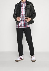 Schwarze Leder-Bikerjacke über einem karierten Hemd, kombiniert mit schwarzen Hosen und weißen Sneakers mit roten Akzenten.