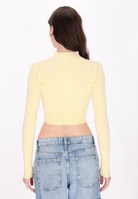 Cropped top giallo a costine con maniche lunghe e collo alto, abbinato a jeans in denim azzurro chiaro a vita alta con tasche posteriori.