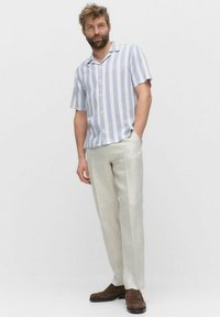 Chemise à manches courtes avec des rayures bleues et blanches, design à boutons. Associée à un pantalon tapered beige clair et des chaussures marron foncé.