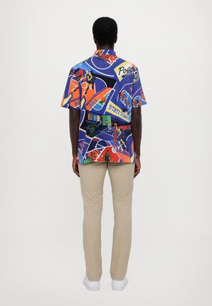 Chemise à manches courtes avec boutons en polyester multicolore, présentant un imprimé graphique sur le thème du basketball avec différents logos et images.