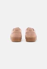 Pink suede sneakers with a rubber sole, featuring a low-top design and embossed branding on the heel. Smooth texture with a clean silhouette.