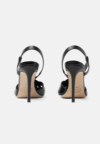 Crne kožne sandale s visokom potpeticom, otvorenim prstima, stražnjim remenom za gležanj i glatkom teksturom. Vitka stiletto potpetica i bež uložak su vidljivi.